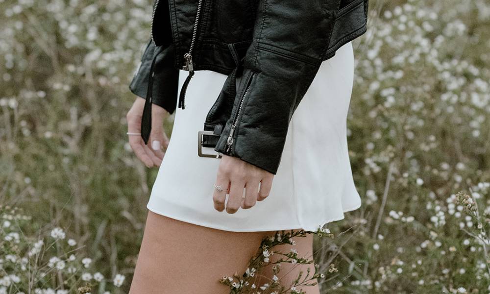 Sea and Silk Events - Amanda McGrath Wedding Planner - Bride at engagement shoot in white dress and black leather jacket in a field of wildflowers - Rosielle and Co